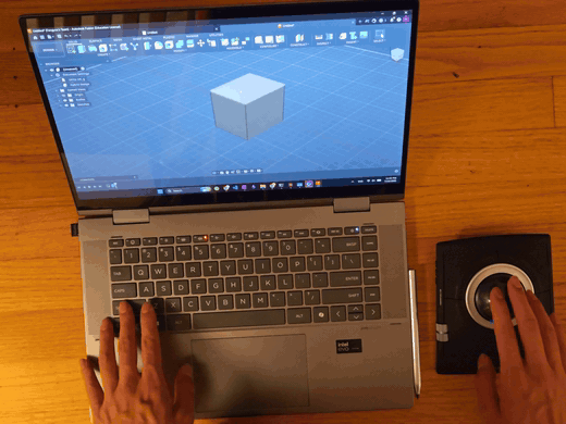 Rolling the trackball with one hand while the model turns in Fusion 360 on the laptop